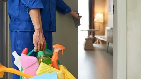 Professional cleaner with bucket of detergents opening room