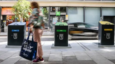 Viandante pasa por delante de contenedores de basura en Madrid - Ayuntamiento de Madrid