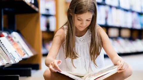 Little girl sitting on the floor and reading books in library