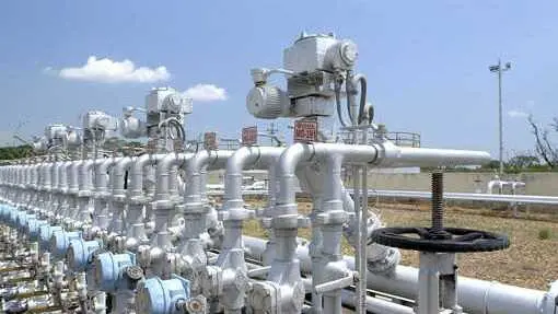 Conjunto de v&aacute;lvulas con tuber&iacute;as plateadas y v&aacute;lvulas azules sobre un campo &aacute;rido y cielo despejado con una nube blanca - Foto de Repsol