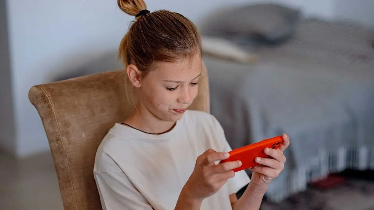 Ni&ntilde;a mirando el tel&eacute;fono m&oacute;vil en su casa - Foto de Lavju de Getty Images