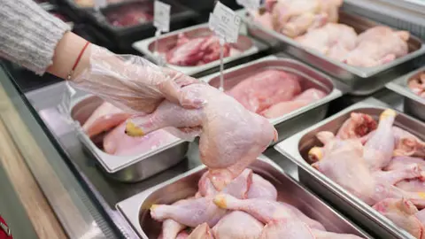 Female hand holding fresh chicken leg quarters in the supermarket.