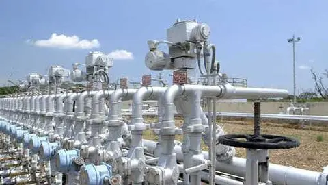 Conjunto de v&aacute;lvulas con tuber&iacute;as plateadas y v&aacute;lvulas azules sobre un campo &aacute;rido y cielo despejado con una nube blanca - Foto de Repsol