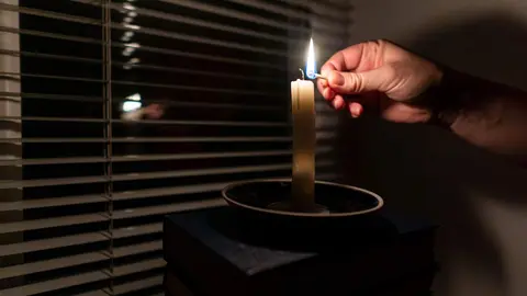 Mujer encendiendo una vela en un apag&oacute;n - Foto de Oleksandr Baranov de Getty Images