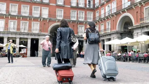 Imagen de archivo de dos turistas caminando con sus maletas por la Plaza Mayor de Madrid